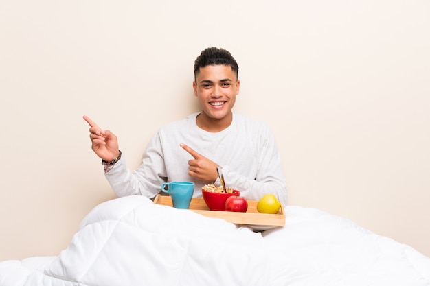 Jovem tomando café da manhã na cama, apontando o dedo para o lado