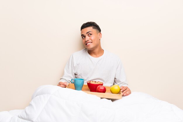 Jovem tomando café da manhã na cama, rindo e olhando para cima