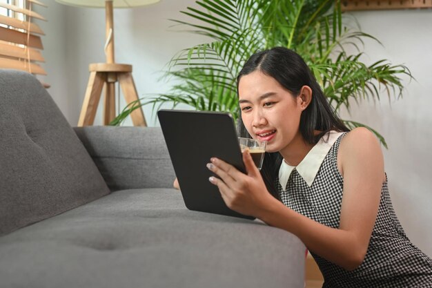 Jovem tomando café e lendo notícias no tablet digital enquanto está sentado na sala de estar