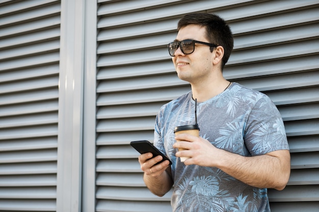 Foto jovem tomando café na cidade e olhando para um telefone móvel