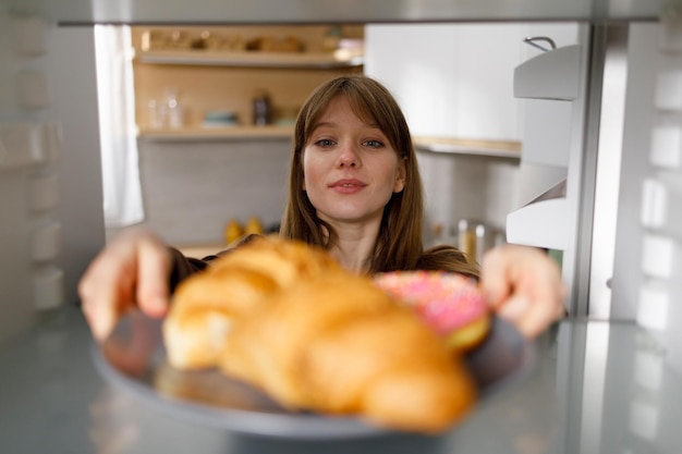 Jovem tomando prato com croissants e rosquinhas da geladeira