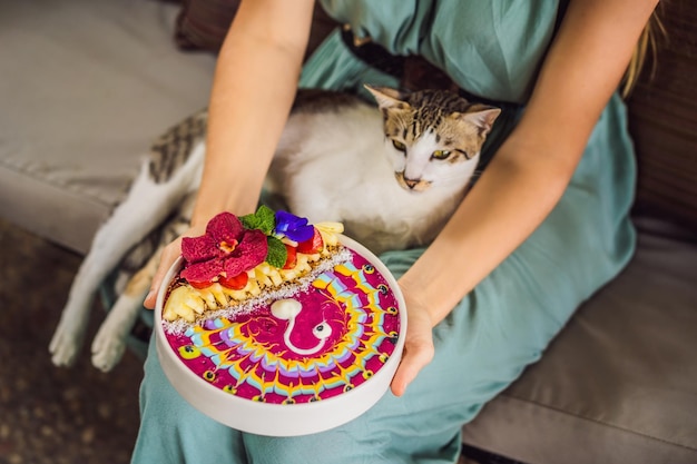 Jovem tomando um café da manhã mediterrâneo sentado em seu sofá e com seu gato e comendo saudável