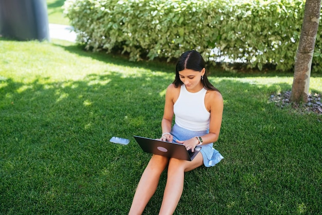 Jovem trabalha com um laptop sentado no gramado