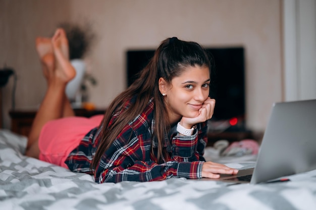 Jovem trabalha enquanto com laptop deitado na cama