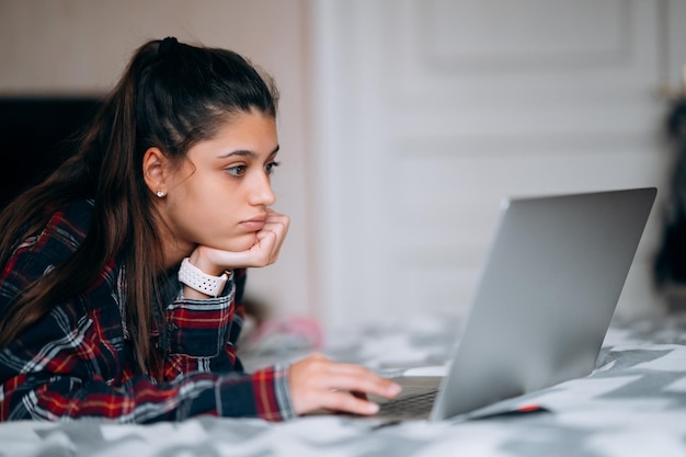 Jovem trabalha enquanto com laptop deitado na cama