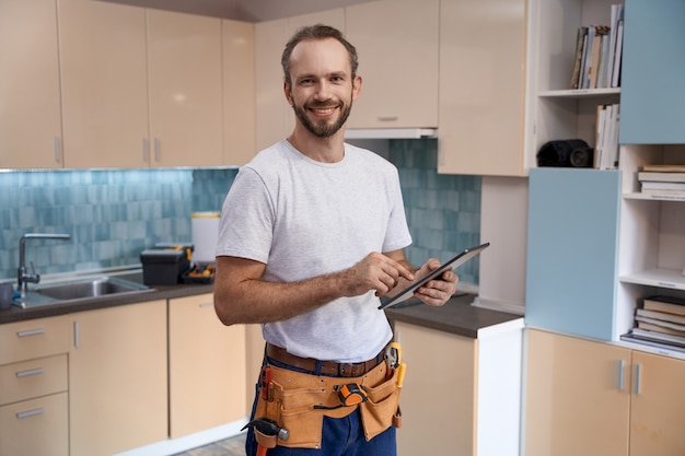 Jovem trabalhador caucasiano do sexo masculino sorridente com tablet durante o trabalho na cozinha