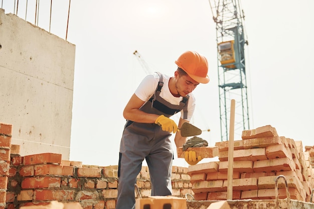 Jovem trabalhador da construção civil de uniforme está ocupado no prédio inacabado