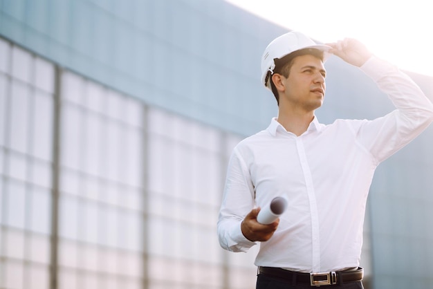 Jovem trabalhador em um capacete e com um telefone em um objeto de trabalho edifício de negócios