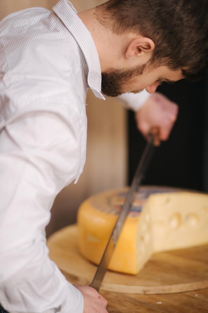 Jovem trabalhador fatia maasdam de queijo na tábua de madeira na loja de queijos