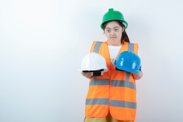 Jovem trabalhadora da construção civil com capacete segurando capacetes sobre uma parede branca