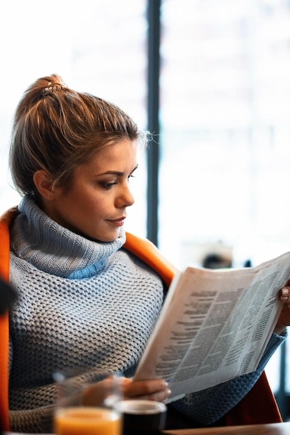 Jovem trabalhadora freelance lendo jornal diário depois do trabalho em um café