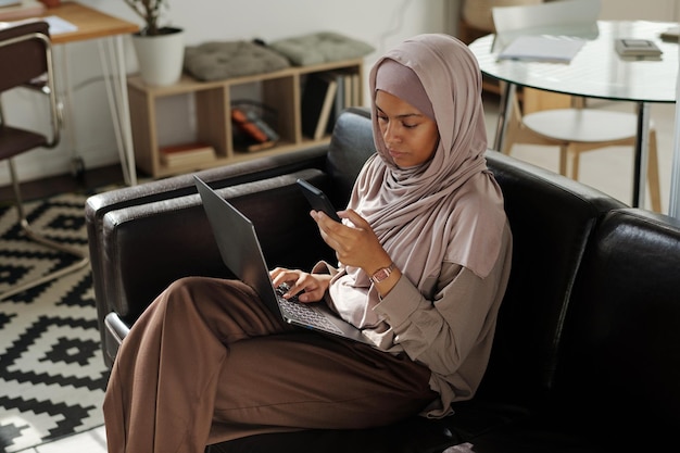 Jovem trabalhadora muçulmana de colarinho branco com laptop de joelhos