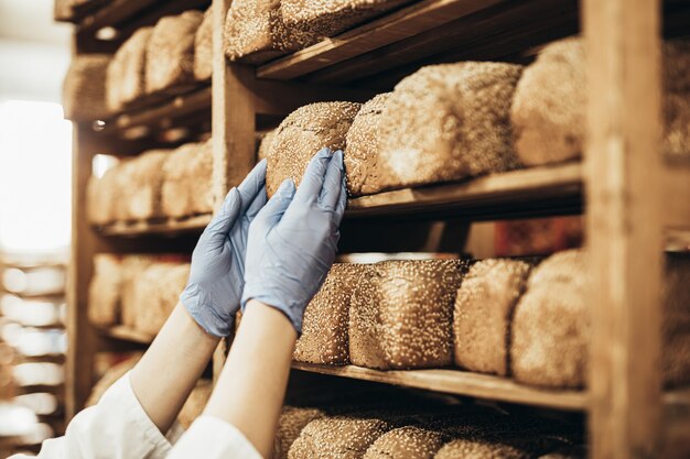 Jovem trabalhadora trabalhando em uma padaria. Ela põe pão na prateleira.