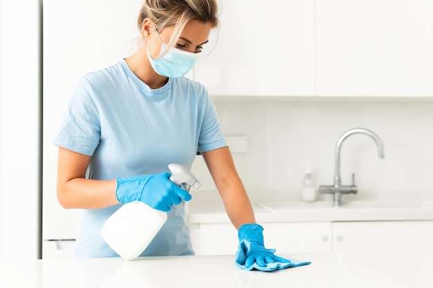 Jovem trabalhadora usando máscara de prevenção e luvas durante a limpeza do apartamento