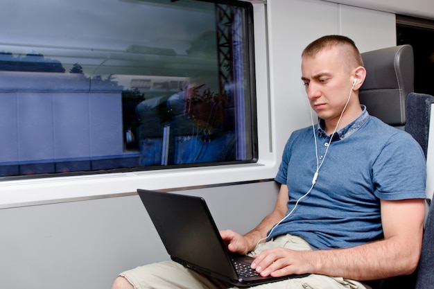 Jovem trabalhando atrás de um laptop, sentado em uma cadeira de trem