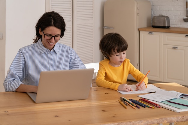 Jovem trabalhando em laptop e filho desenhando