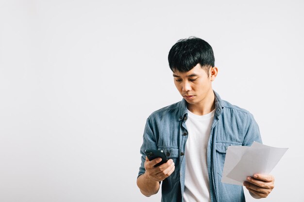 Jovem trabalhando em papelada financeira segurando contas e respondendo a uma chamada de telefone celular sua expressão claramente preocupada e chateada com as despesas financeiras Isolado em branco