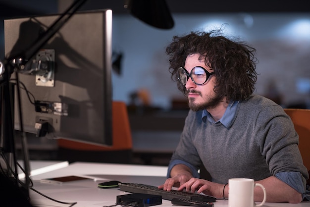 Foto jovem trabalhando no computador à noite no escritório de inicialização escuro. o designer trabalha mais tarde.