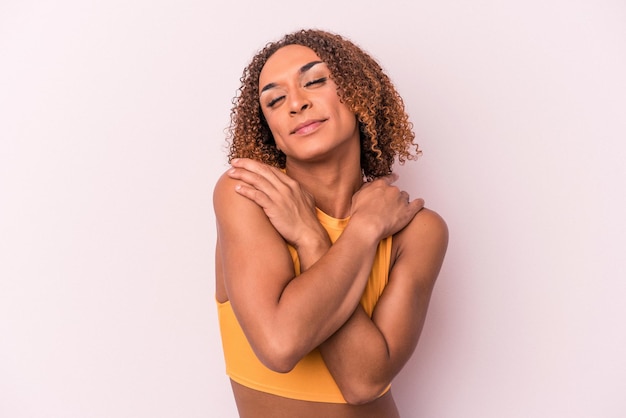 Foto jovem transexual latina isolada em abraços de fundo rosa, sorrindo despreocupado e feliz.