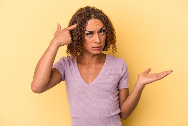 Foto jovem transexual latina isolada em fundo amarelo, mostrando um gesto de decepção com o dedo indicador.