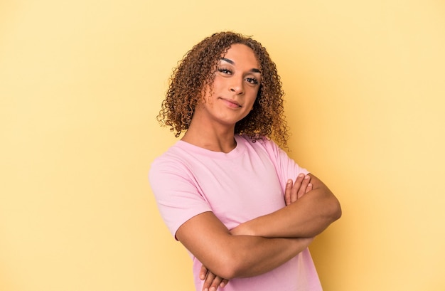 Jovem transexual latina isolada em fundo amarelo que se sente confiante, cruzando os braços com determinação.