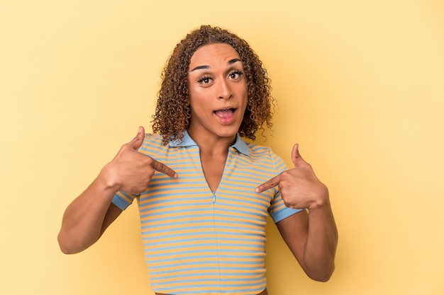 Jovem transexual latina isolada em fundo amarelo surpreendeu apontando com o dedo, sorrindo amplamente.