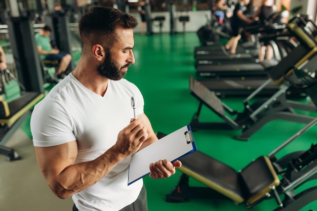 Jovem treinador fazendo um plano de treinamento em uma academia Copie o espaço