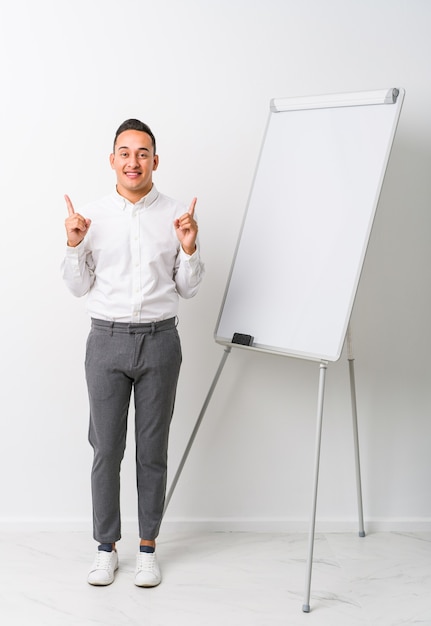 Jovem treinador latino com um quadro branco isolado indica com os dois dedos anteriores mostrando um espaço em branco.