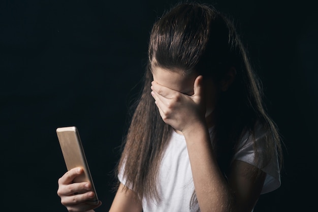 Jovem triste e vulnerável usando telefone celular assustada e desesperada sofrendo abuso on-line cyberbullying sendo perseguida e assediada no conceito de cyberbullying adolescente