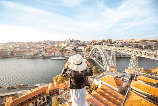 Jovem turista apreciando a bela paisagem da cidade velha com o rio e a famosa ponte de ferro durante o pôr do sol na cidade do Porto, Portugal