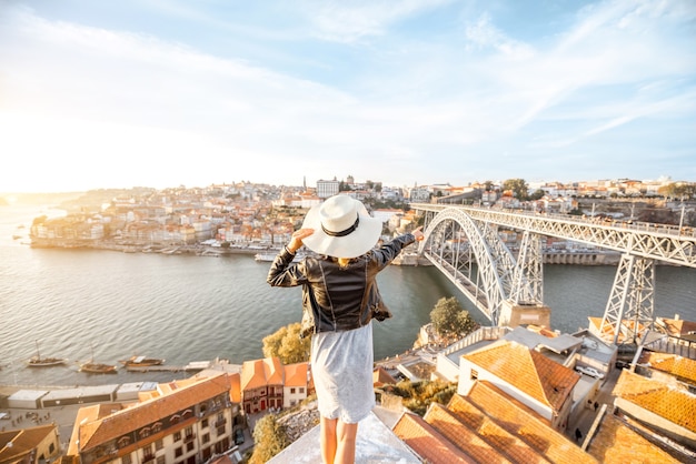 Jovem turista apreciando a bela paisagem da cidade velha com o rio e a famosa ponte de ferro durante o pôr do sol na cidade do Porto, Portugal