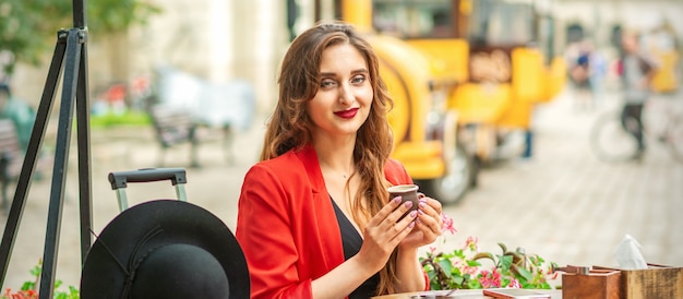 Jovem turista caucasiana com casaco vermelho com uma xícara de café à mesa no café ao ar livre.