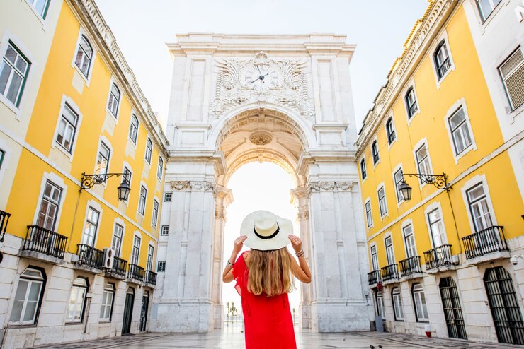 Foto jovem turista com um vestido vermelho em pé em frente ao famoso arco do triunfo no centro da cidade de lisboa, em portugal