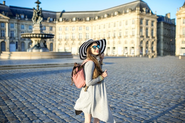 Jovem turista em pé na famosa praça Bourse com belos edifícios e uma fonte na cidade de Bordeaux durante a manhã