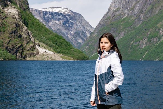 Jovem turista em primeiro plano e atrás dela o fiorde com as altas montanhas em Gudvangen Noruega