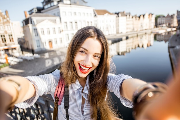 Jovem turista fazendo selfie em pé na ponte com uma bela vista da cidade de Gent, na Bélgica