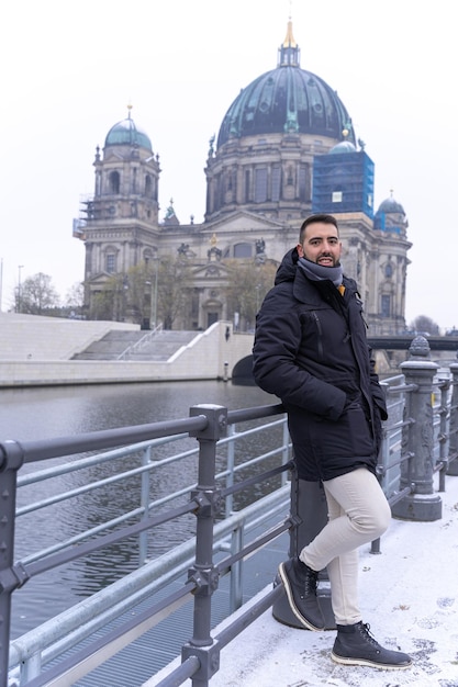 Jovem turista masculino barbudo encostado na cerca do rio com a Catedral de Berlim ao fundo Alemanha