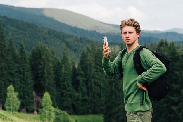 Jovem turista masculino em roupas casuais e com uma mochila em pé em um prado de montanha