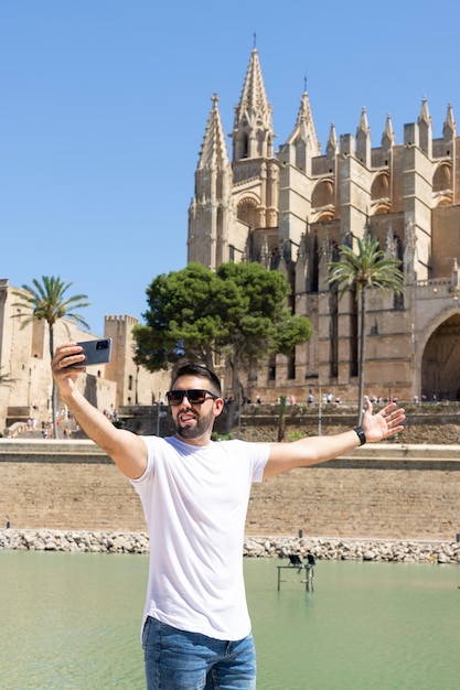 Jovem turista masculino fotografando-se em frente à catedral de Palma de Maiorca em um dia ensolarado na Espanha
