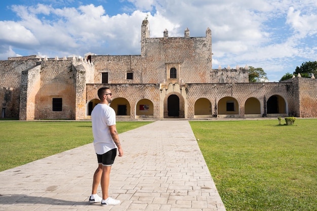 Jovem turista masculino posando de costas para o lado de fora do Convento de San Bernardino com o gramado verde bem cuidado em Valladolid México