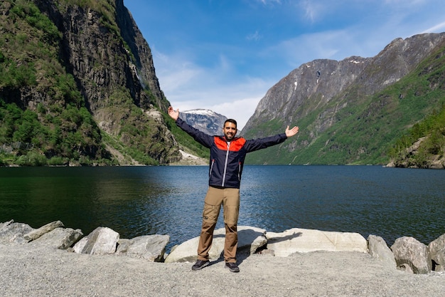 Jovem turista no sopé do fiorde com os braços para cima cercado por altas montanhas em Gudvangen Noruega