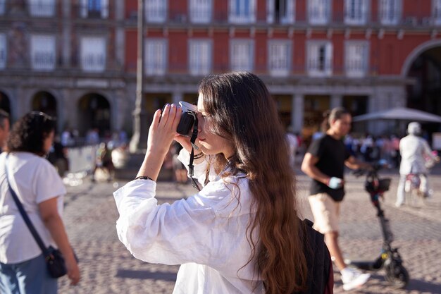 Jovem turista segurando uma câmera e tirando uma foto na Plaza Mayor Madrid Espanha