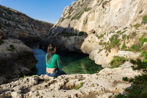 Jovem turista sentada olhando para Wied IlGhasri em Gozo Malta