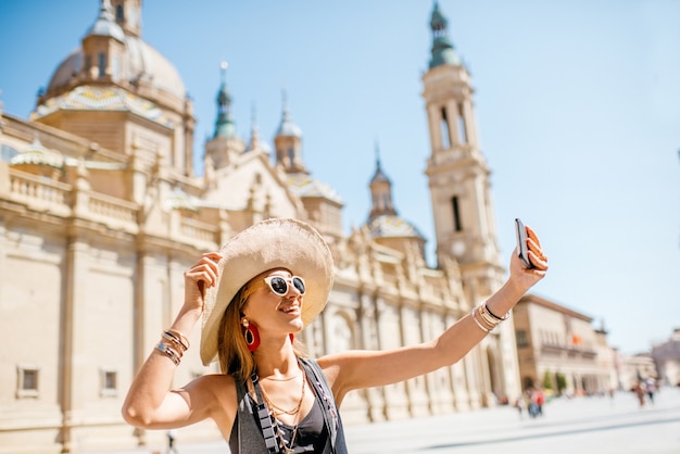 Jovem turista tirando fotos de selfie em frente à famosa catedral na praça central durante o tempo ensolarado na cidade de Zaragoza, Espanha