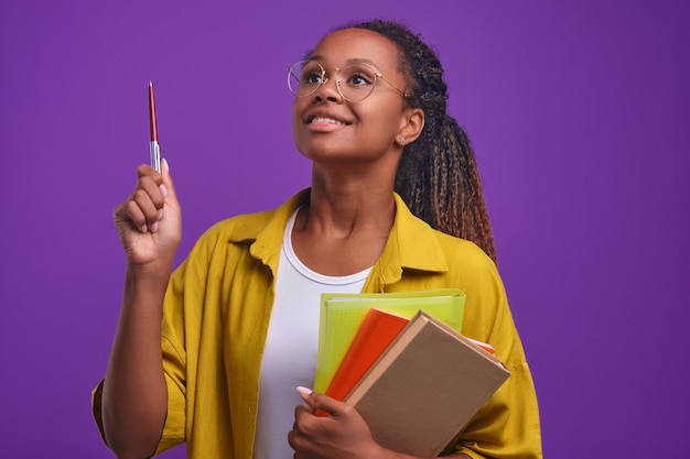 Foto jovem tutora afro-americana orgulhosa com pastas de trabalho na mão levanta a caneta