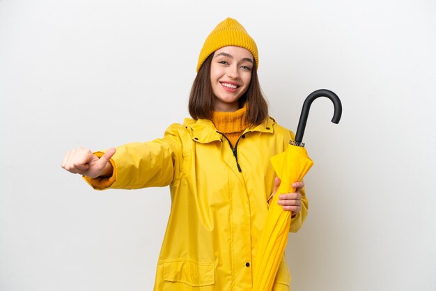 Jovem ucraniana com casaco à prova de chuva e guarda-chuva isolado no fundo branco dando um polegar para cima gesto