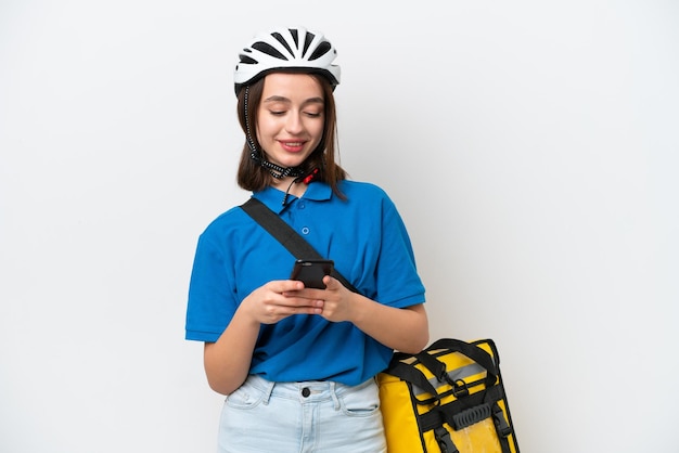 Jovem ucraniana com mochila térmica isolada em fundo branco enviando uma mensagem com o celular