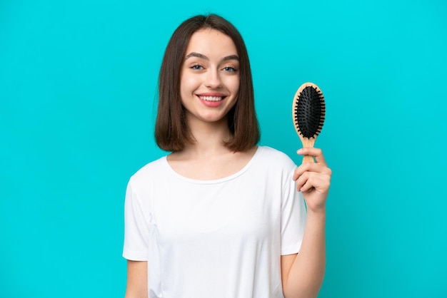 Jovem ucraniana com pente de cabelo isolado em fundo azul sorrindo muito