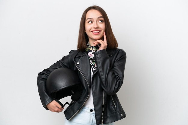 Jovem ucraniana com um capacete de moto isolado em fundo branco pensando em uma ideia enquanto olha para cima