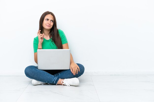 Jovem ucraniana com um laptop sentado no chão com dedos cruzando e desejando o melhor